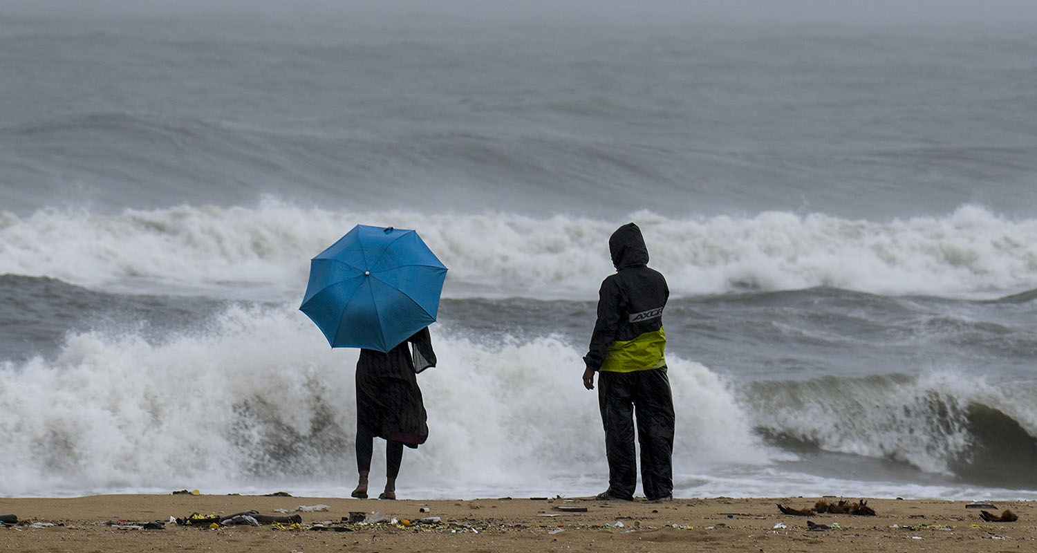 People look at the rough sea amid rainfall due to Cyclone Ditwah at Marina Beach, in Chennai, on Monday.